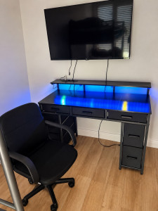 Photo de galerie - Installation complète d’un espace bureau : montage du bureau et de la chaise, fixation murale de la télévision et mise en place de l’ensemble.