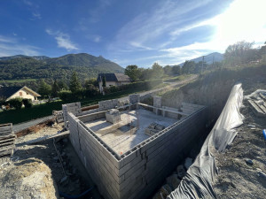 Photo de galerie - Élévation des murs en parpaings en cours, chantier propre avec dalle déjà réalisée et murs du rez-de-chaussée en montage.