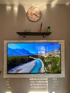 Photo de galerie - Installation TV murale avec fixation sécurisée, création d’un cadre effet marbre sur mesure autour de l’écran et pose d’étagère murale. Travail propre et finitions soignées.