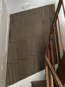Photo de galerie - Pose de panneaux décoratifs à tasseaux de bois sur fond noir dans une cage d’escalier, pour un rendu moderne et chaleureux. 