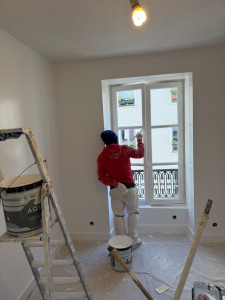 Photo de galerie - Un peintre en bâtiment professionnel en train de peindre soigneusement une fenêtre dans un intérieur propre et lumineux. 