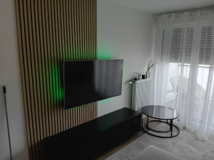 Photo de galerie - Montage d'un meuble TV, fixation du support mural et installation du téléviseur, ainsi que pose de panneaux muraux en tasseaux de bois décoratifs.