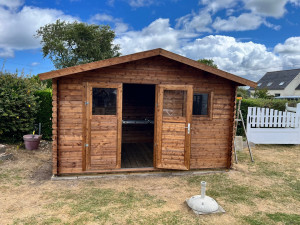 Photo de galerie - Montage complet de l’abri de jardin en bois, installation du plancher, assemblage des panneaux et fixation de la structure, avec mise en place des portes vitrées. L’ensemble est posé solidement sur sa base et finalisé avec des finitions propres