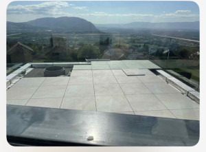 Photo de galerie - Pose de dalles céramiques grand format sur terrasse panoramique : étanchéité, plots/colle, réglage au laser et maillet, garde-corps en verre pour la sécurité et la vue.