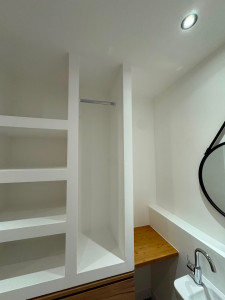 Photo de galerie - Aménagement sur mesure en placo dans une salle d’eau avec niches de rangement, espace penderie, tablette en bois, éclairage intégré et mise en peinture. Travail réalisé avec des finitions très soignées et un rendu parfaitement intégré à la pièce.