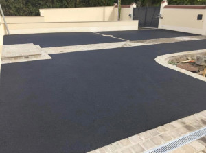 Photo de galerie - Réalisation ALV : Cour carrossable complète.
 Travaux : Préparation du sol, application d'un enrobé noir à chaud, pose de lignes de pavés décoratifs, et installation du système de drainage avec caniveau pour les eaux de pluie. Devis gratuit !
