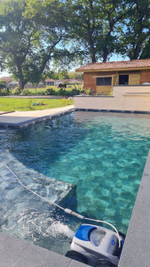 Photo de galerie - Création piscine avec plage arrondie et escalier, jardinières surélevées avec cascades et en arrière plan une cuisine d'été de 24m2 en bois sur plots béton ainsi qu'un boulodrome