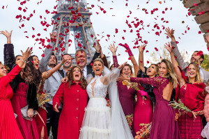 Photo de galerie - Scène festive d’un mariage à Paris, avec des invités en tenue élégante lançant des pétales de rose devant la Tour Eiffel. L’ambiance est joyeuse, colorée et pleine de célébration.