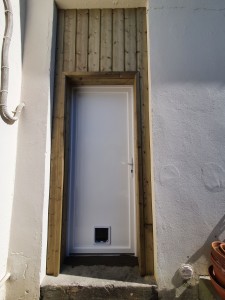 Photo de galerie - Dépose d'une porte vétuste en verre et bois avec fenêtre sur le dessus, création d'un châssis sur mesure pour accueillir la nouvelle porte en pvc, mise en place d'une chatière, habillage bois sur l'extérieur 