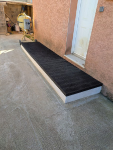 Photo de galerie - Petite terrasse d'entrée réalisée avec une base maçonnée et couverte avec des lames en composite.