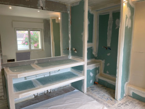 Photo de galerie - Création d’une structure en plaques hydrofuges avec meuble double vasque intégré, niches de rangement et préparation de l’espace douche. Travail précis avec finitions des bandes pour un support prêt à recevoir le carrelage.