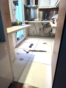 Photo de galerie - Remplacement d'un vieux linoléum usé dans une cuisine. Il a fallu retirer tous les éléments bas, démonter des éléments fixés. Le sol n'était pas plan, il a fallu également refaire une chape avant la pose de grandes dalles de 60x60 cm en céramique blanche.