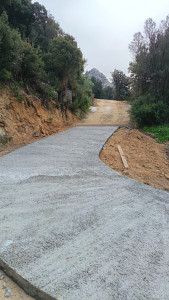 Photo de galerie - Une allée/rampe en béton récemment réalisée dans un environnement naturel et boisé.
Le béton est encore frais avec une finition antidérapante, adaptée aux accès en pente. Le chemin suit une légère courbe et monte vers une piste en terre située plus haut.