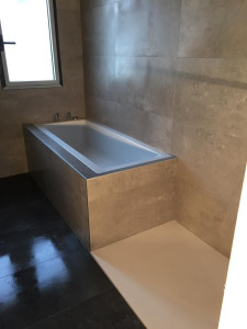 Photo de galerie - Une salle de bain moderne en finition, avec une baignoire encastrée habillée de grands carreaux effet pierre et un espace douche à l'italienne attenant.