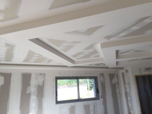 Photo de galerie - Réalisation d'un plafond en plaques de plâtre avec retombées décoratives et éclairage indirect. Pose de placo, traitement des bandes à joints, ratissage et préparation des supports avant peinture. Travail soigné avec des finitions de qualité.