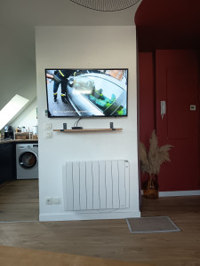 Photo de galerie - Mise en place de la TV dans le salon sur support mural orientable avec étagères pour accessoires TV 
