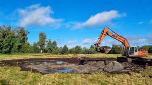 Photo de galerie - Création d'une mare en prairie : excavation, mise en forme du bassin et modelage des berges à la pelle mécanique.