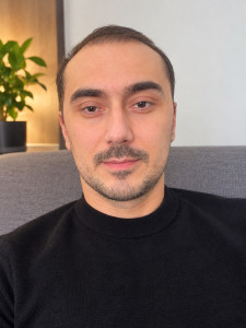 Photo de galerie - Portrait moderne et réaliste d’un homme en pull noir, en gros plan, avec un éclairage doux et chaleureux. Expression naturelle, arrière-plan intérieur élégant avec effet bokeh, qualité professionnelle.