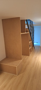 Photo de galerie - Fabrication et installation d’un dressing en bois sur mesure sous l’escalier, adapté à la forme de l’espace.