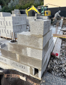 Photo de galerie - Mise en œuvre des blocs de maçonnerie pour la réalisation des fondations et du soubassement, avec pose des armatures en acier en vue du renforcement de la structure.