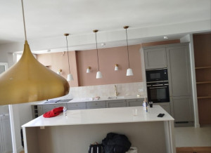 Photo de galerie - Installation et assemblage complet d'une cuisine en kit avec îlot central : montage des meubles, ajustement des éléments et installation des luminaires suspendus. Travail soigné et finitions impeccables.