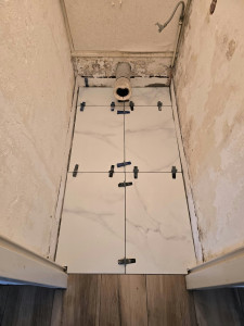Photo de galerie - Rénovation et pose de carrelage effet marbre blanc au sol des toilettes. Utilisation d'un système de nivellement de précision pour assurer des joints parfaits et une surface plane, avec une attention particulière aux détails techniques de plomberie et d'é