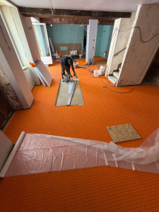 Photo de galerie - Pose de la natte de désolidarisation sur l’ensemble de la surface du plancher, en préparation de l’installation du système de chauffage au sol par cordon chauffant.