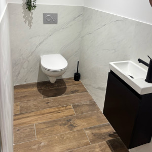 Photo de galerie - Réalisation d’un WC avec carrelage imitation bois au sol et faïence effet marbre sur les murs. Association élégante pour un rendu moderne, propre et chaleureux. ?