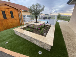 Photo de galerie - Création d'une jardinière, habillage pierre de parement silver crème et couvertine en travertin. Pose d'un gazon synthétique. plantation et galet décoratif 