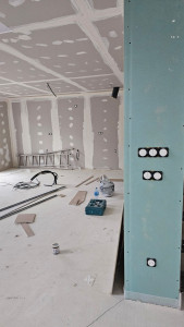 Photo de galerie - Cuisine en arrière plan avec la prise hotte, les doubles prises plan de travail, prise four, frigo et îlot central.