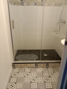Photo de galerie - Rénovation d'une douche à l'italienne : carrelage mural blanc avec frise décorative, receveur de douche noir. Travail propre et étanchéité parfaite.