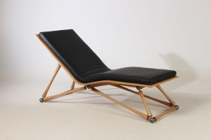 Photo de galerie - Chaise longue avec son assise cintrée en chêne, habillée de son coussin en cuir de vahette, supportée par un piètement métallique recouvert de pièce tournée en chêne