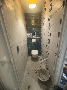 Photo de galerie - Travaux de carrelage dans une salle de bain en rénovation. Pose de carrelage mural avec finitions soignées et préparation des surfaces avant la phase finale.