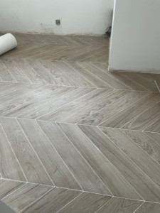 Photo de galerie - Pose de carrelage imitation bois en chevrons, avec une finition soignée et des découpes précises. Travail réalisé avec soin pour un rendu moderne et élégant.
