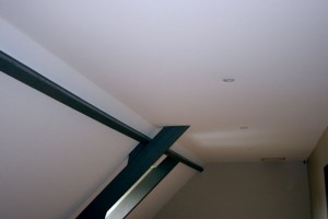 Photo de galerie - Plafond Tendu à froid.
Contournement poutres et intégration de spots.
Toile textile tendue à froid 