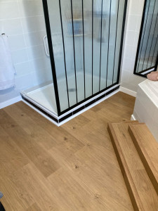 Photo de galerie - Pose de lames pvc dans une salle de bain après ragréage avec habillage des marches de la baignoire d’angle.