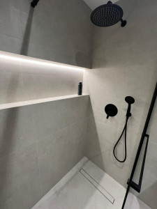 Photo de galerie - Rénovation douche à l'italienne : pose de grand carrelage gris effet pierre, robinetterie encastrée noire mate et niche rétroéclairée par LED intégrée. Un design épuré et moderne.