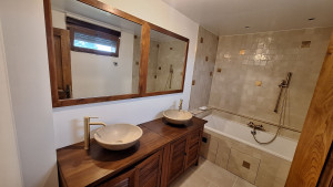 Photo de galerie - Salle de bain moderne et élégante, avec double vasque en pierre, meuble en bois et baignoire avec douche. Atmosphère chaleureuse et raffinée.