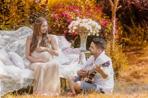 Photo de galerie - Un couple partage des moments d’amour et de complicité lors d’une séance photo de maternité en plein air, entouré de fleurs et de lumière douce