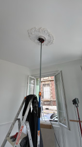 Photo de galerie - Pose d’une rosace en polystyrène au plafond (la photo montre la rosace en cours de fixation)
