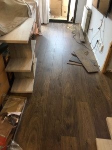 Photo de galerie - Installation complète d’un parquet stratifié avec découpes précises et finitions soignées. Alignement parfait des lames pour un rendu moderne et chaleureux.