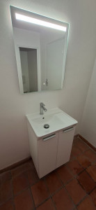 Photo de galerie - Mise en place d'un meuble vasque avec la vasque, le robinet et le système d'évacuation et le miroir.