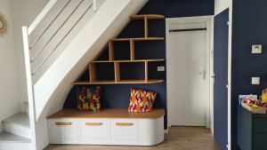 Photo de galerie - Meuble banc sur-mesure avec tablettes suspendu pour bibliothèque (fixation invisible).
Recouvrement avec panneaux peint du dessous de l'escalier.