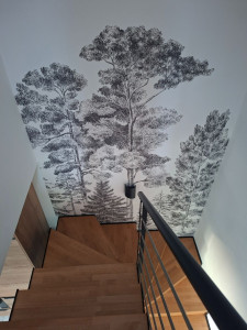 Photo de galerie - Habillage complet d'une cage d'escalier à La Rochelle avec un papier peint panoramique motif forêt en noir et blanc. Un résultat spectaculaire qui sublime un espace souvent négligé.