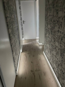 Photo de galerie - Pose de plinthes intégrant un éclairage LED indirect dans un couloir : ajustement et coupe des angles, intégration discrète du ruban LED, raccordement sur prise existante. Lumière douce
  mettant en valeur le revêtement de sol.