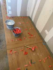 Photo de galerie - Pose de carrelage en cours de réalisation, imitation parquet, avec système de nivellement pour une surface parfaitement plane et des joints réguliers. Travail soigné et découpes propres. 