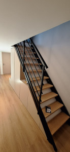 Photo de galerie - Fabrication et installation d’un dressing en bois sur mesure sous l’escalier, adapté à la forme de l’espace.