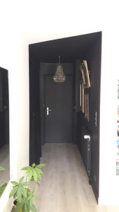 Photo de galerie - Une entrée d'appartement peinte en noir avec un trait oblique au plafond qui part de la cloison à droite vers la penderie à gauche