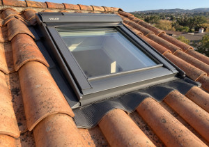 Photo de galerie - Pose d’une fenêtre de toit Velux sur une toiture en tuiles canal, avec installation des raccords d’étanchéité pour assurer une bonne protection contre les infiltrations d’eau.