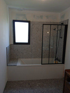 Photo de galerie - Pose d'éléments de salle de bain (maison neuve). Sol PVC, revêtement mural PVC, baignoire avec raccordement sanitaire, pare baignoire et tablier en carrelage blanc.